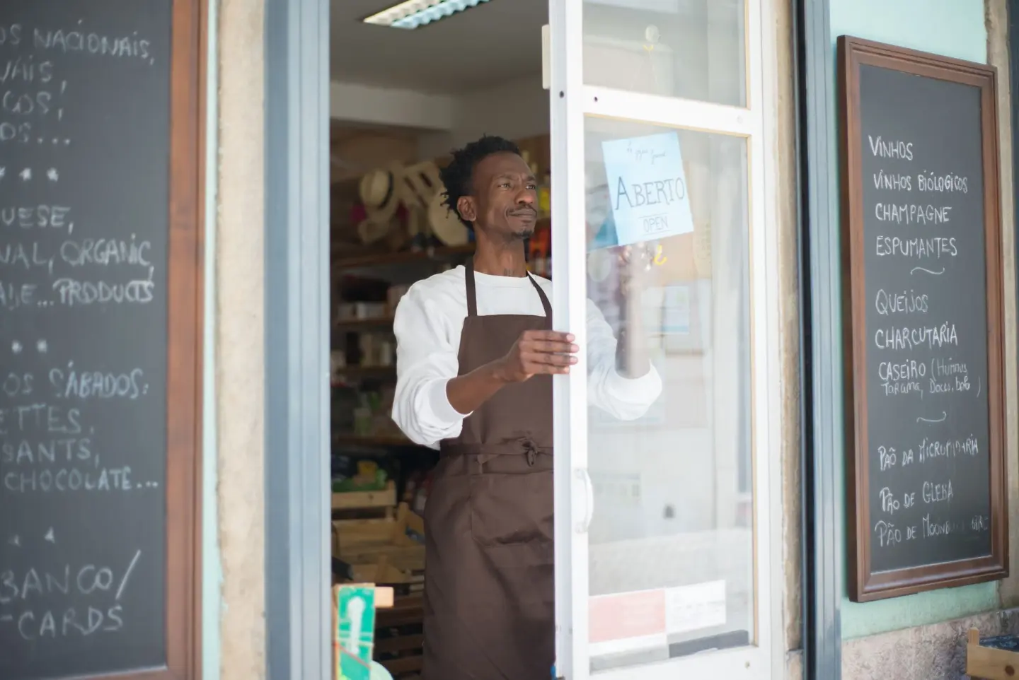 A man in an apron opens a grocery store door in Portugal, ready for business.