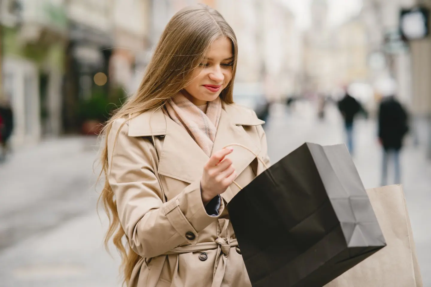 Caucasian woman smiling outdoors with shopping bags in winter attire.